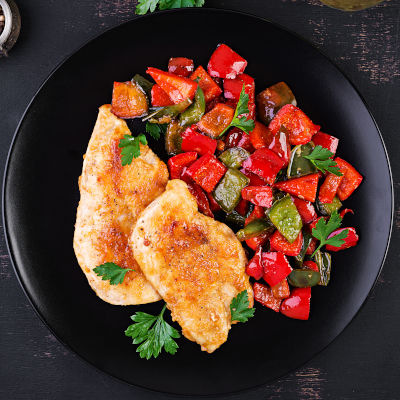 Grilled chicken fillets and sweet pepper on black plate. Top view, copy space